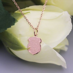 May include: A rose gold necklace with a small, detailed shield pendant. The pendant is a delicate, intricate design.