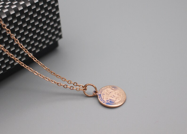 May include: A rose gold chain necklace with a round pendant featuring a detailed image of Saint Michael the Archangel. The pendant has the words "Saint Michael" inscribed around the edge.