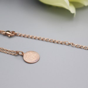 May include: A rose gold necklace with a delicate chain and a round pendant featuring the word "Chanel" engraved on it.