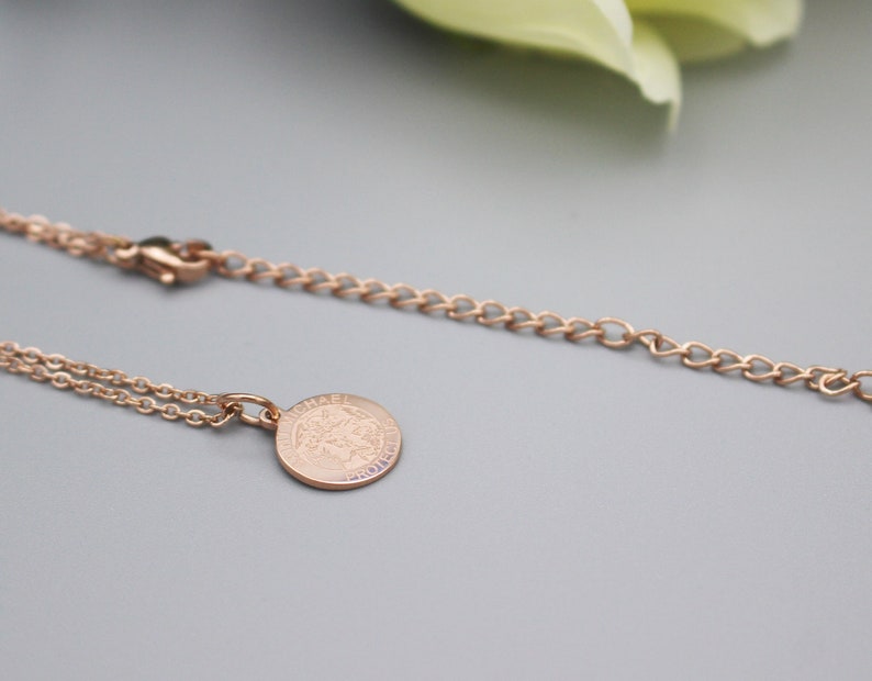 May include: A rose gold necklace with a delicate chain and a round pendant featuring the word "Chanel" engraved on it.