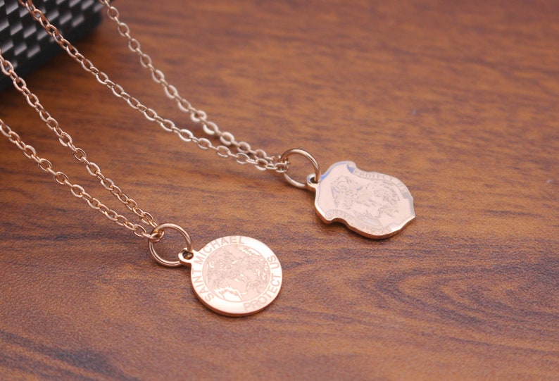 May include: Two gold necklaces with pendants. One pendant is round and says "Saint Michael Protect Us". The other pendant is a shield shape with an image of an angel.