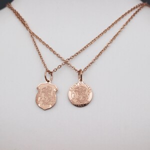May include: Two gold necklaces with pendants. One pendant is a shield with a religious figure and the other is a round pendant with the words "Saint Michael Protect Us".