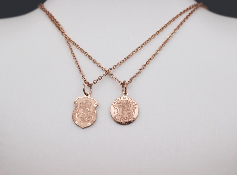 May include: Two gold necklaces with pendants. One pendant is a shield with a religious figure and the other is a round pendant with the words "Saint Michael Protect Us".