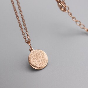 May include: A rose gold chain necklace with a round pendant featuring the words "Saint Michael Protect Us".