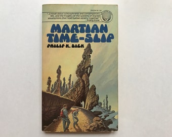 May include: A book cover with a colorful illustration of a rocky landscape with two figures walking towards a cave. The title of the book is "MARTIAN TIME-SLIP" by Philip K. Dick.