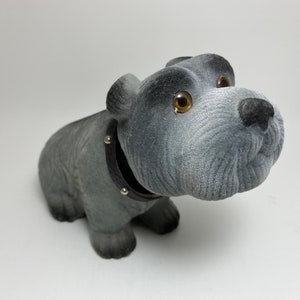 May include: A grey plush toy dog with a black studded collar. The dog is sitting with its head tilted to the side and its eyes open.