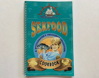 May include: A teal blue cookbook with a yellow circle featuring a boy holding a fish. The title is "Westcoaster's Seafood A Westcoaster's Treasured Collection Cookbook".