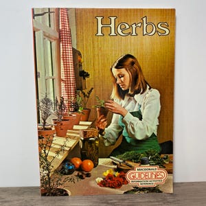 May include: A vintage book cover titled "Herbs" showing a woman with a potted herb plant. The cover has a warm colour palette with a window, plants, and the text "Macdonald Guidelines".