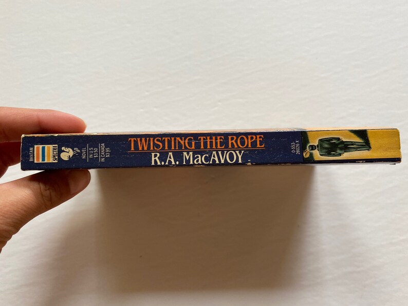 Puede incluir: Un libro de bolsillo azul con el t&iacute;tulo "Twisting the Rope" de R.A. MacAvoy. La portada del libro presenta la silueta de una persona con traje.