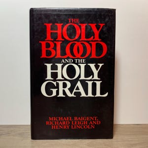 May include: A black hardcover book with the title "THE HOLY BLOOD AND THE HOLY GRAIL" in red and white lettering. The authors' names, Michael Baigent, Richard Leigh, and Henry Lincoln, are printed at the bottom of the book.