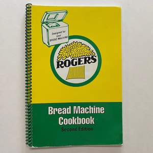 May include: A green and yellow spiral bound cookbook titled "Bread Machine Cookbook, Second Edition". The cover features a green and white logo with the word "ROGERS" and a wheat stalk design.