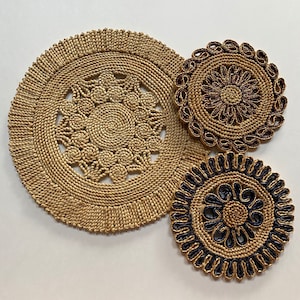 May include: Three woven straw coasters with intricate designs. The largest coaster is natural brown with a circular pattern. The two smaller coasters have a black and brown design with a circular pattern.