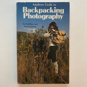 以下が含まれることがあります： テッド・シフマンとスーザン・ラリビエールによる「Amphoto Guide to Backpacking Photography」というタイトルの本。表紙には、バックパックを背負って背の高い草のフィールドで写真を撮っている人が写っています。