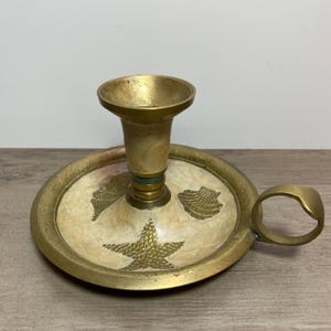 May include: Brass candlestick with a white base featuring a starfish and seashells. The candlestick has a handle and a green band around the top of the candle holder.