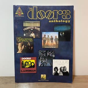 May include: A blue anthology book featuring album covers by The Doors. The book's cover includes the band's logo in gold, and the album titles "Morrison Hotel", "L.A. Woman", and "Other Voices". The book is published by Hal Leonard.
