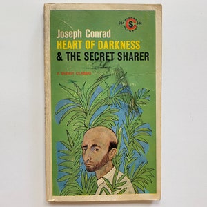 May include: A green paperback book cover with the title "Joseph Conrad HEART OF DARKNESS & THE SECRET SHARER" and a drawing of a man with a beard in front of a jungle.