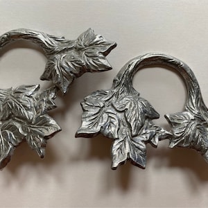 May include: Two silver metal napkin rings shaped like a vine with leaves. The rings are connected together.