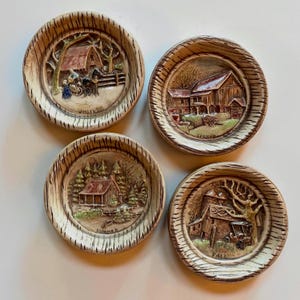 May include: A set of four round ceramic plates featuring embossed seasonal scenes. Each plate has a textured wood-grain border and depicts a landscape labeled Winter, Spring, Summer, or Fall, showcasing houses, trees, and vehicles in muted tones.