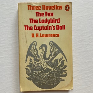 May include: A vintage paperback book cover with a yellow background and a black and white illustration of a bird. The title is "Three Novellas" by D.H. Lawrence. The novellas are "The Fox", "The Ladybird", and "The Captain's Doll".