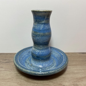 May include: A blue and white ceramic candle holder with a wide base and a tall, slender top. The holder has a swirling pattern of blue and white glaze.