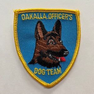 May include: A blue and yellow embroidered patch with a German Shepherd dog's head and the text "Oakalla Officer's Dog Team".