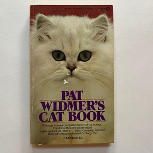 May include: A book cover featuring a white Persian cat on the front. The title of the book is "Pat Widmer's Cat Book". The book cover is red with a purple border.