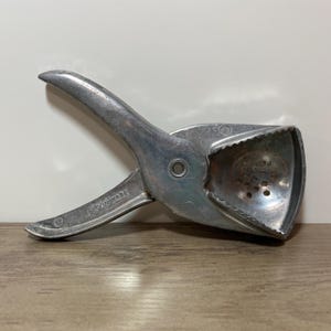 May include: A vintage silver-colored citrus juicer with a hinged design. The juicer has a handle and a bowl-shaped press with drainage holes. The text "IRVIN WARE" is visible on the handle. The juicer is designed to extract juice from citrus fruits.