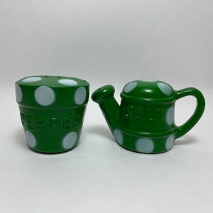 May include: Green and white polka dot salt and pepper shakers. The pepper shaker is shaped like a flower pot and says "Pepper" on the side. The salt shaker is shaped like a watering can and says "Salt" on the side.