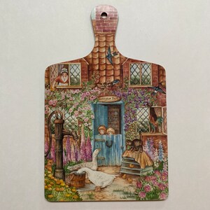 May include: A wooden chopping board with a painted scene of a cottage with a well, flowers, and birds. The text "Horseshoe Farm" is painted on the cottage.