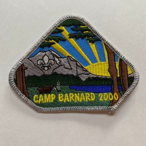 May include: An embroidered triangular patch depicting a mountain scene, a lake, trees, and a sunrise. The text "CAMP BARNARD 2000" is embroidered in yellow at the bottom.
