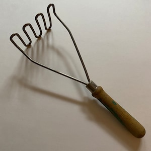 May include: A vintage metal potato masher with a wooden handle. The handle is painted with a light blue and green design.