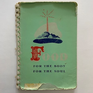 以下が含まれることがあります： 螺旋状の綴じ込みが施された緑色のビンテージの料理本。表紙には、塔のある家のスタイリッシュなイラストと、赤と白の文字で「FOOD」という言葉が描かれています。「FOR THE BODY FOR THE SOUL」というテキストがイラストの下に印刷されています。