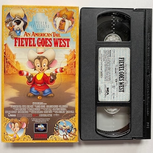 May include: A VHS tape case for the animated film An American Tail: Fievel Goes West. The front of the case features a cartoon mouse wearing a red vest and holding a pair of pistols. The text "An American Tail: Fievel Goes West" is printed in large, bold letters on the case.