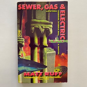 May include: A book cover with a colorful, abstract design featuring a submarine, a shark, and a sewer grate. The title is "Sewer, Gas & Electric: The Public Works Trilogy" by Matt Ruff.