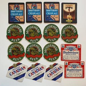 May include: A collection of beer coasters featuring various brands. The coasters include "Shaftebury Cream Ale", "Moosehead Beer", "Budweiser Premium Beer", and "Molson Canadian Lager Beer". The coasters are in various shapes and colors.