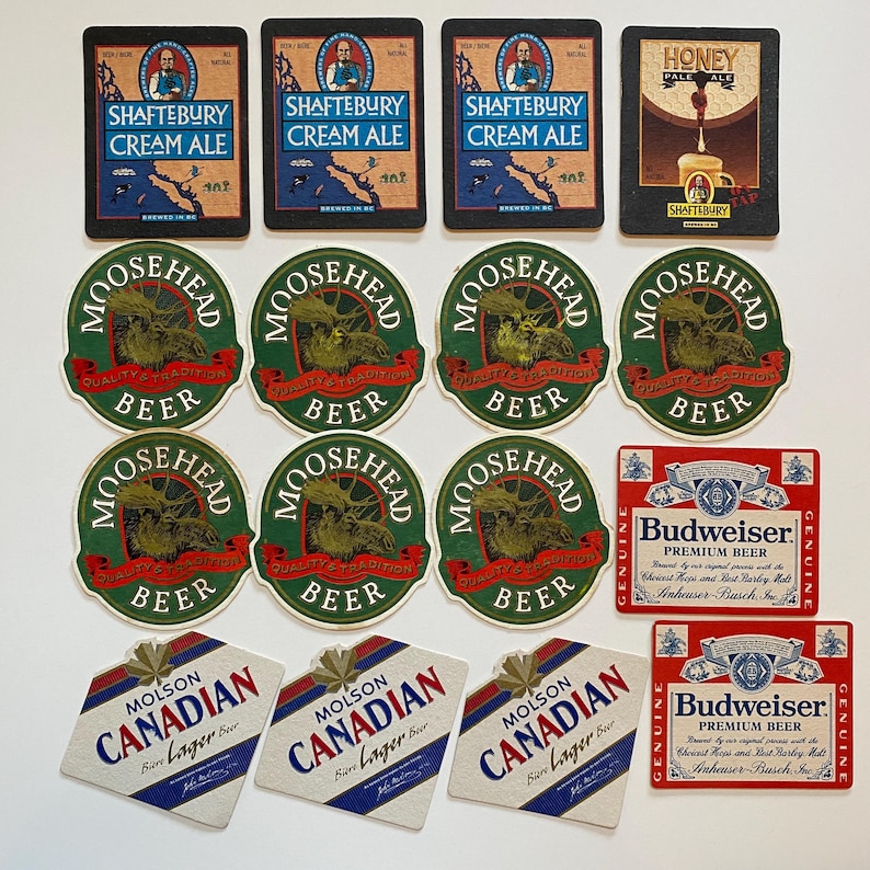 May include: A collection of beer coasters featuring various brands. The coasters include "Shaftebury Cream Ale", "Moosehead Beer", "Budweiser Premium Beer", and "Molson Canadian Lager Beer". The coasters are in various shapes and colors.