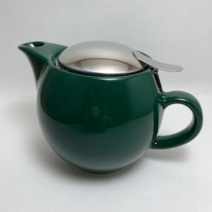 May include: A green ceramic teapot with a stainless steel lid and a built-in strainer. The teapot has a round body and a handle on the side.