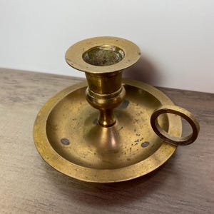 Peut inclure: Un chandelier en laiton avec une base ronde et une poignée en forme d'anneau. Le chandelier a une finition usée et antique.