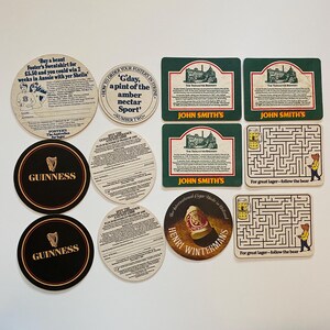 May include: A collection of vintage beer coasters featuring various brands and designs. Includes Guinness, John Smith's, and Foster's. Some coasters have text, including a maze with a bear and the phrase "For great lager - follow the bear."