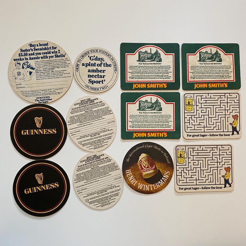 May include: A collection of vintage beer coasters featuring various brands and designs. Includes Guinness, John Smith's, and Foster's. Some coasters have text, including a maze with a bear and the phrase "For great lager - follow the bear."
