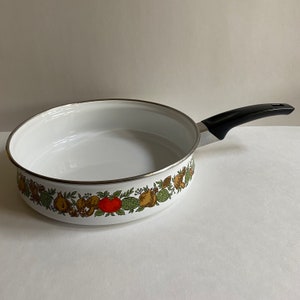 May include: White enamel saucepan with a black handle and a colourful floral design around the rim. The design features green leaves, brown and yellow fruits, and red tomatoes.