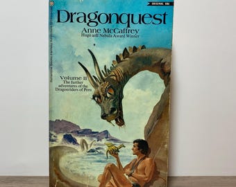 May include: Vintage paperback book titled "Dragonquest" by Anne McCaffrey. The cover features a fantasy illustration of a dragon and a man holding a small dragon. The book is Volume II of "The further adventures of the Dragonriders of Pern."