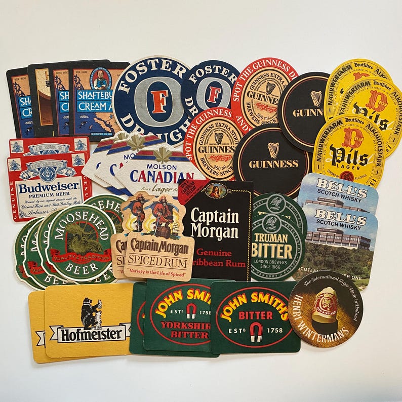 May include: A collection of vintage beer and liquor coasters featuring various brands. The coasters are in various shapes and colors, including red, green, black, and yellow. Brands include Guinness, Budweiser, and Captain Morgan.