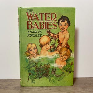 May include: A hardcover book titled The Water Babies by Charles Kingsley with a green cover featuring an illustration of four children swimming in water with fish and seaweed. The title and author name are printed in dark red lettering.