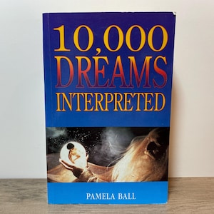 May include: A book titled "10,000 Dreams Interpreted" with a blue cover and yellow and red lettering. The cover features an illustration of a person holding a crystal ball with a figure inside. The author's name, Pamela Ball, is at the bottom.
