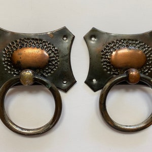Peut inclure: Deux poignées de porte ou d'armoire anciennes en cuivre et métal vert avec des poignées en anneau. Les poignées ont une texture martelée et un ovale en cuivre au centre.