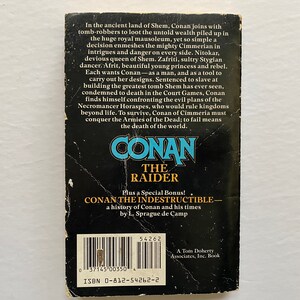 Może przedstawiać: Czarno-biała okładka książki z tytułem "Conan The Raider" w dużych, pogrubionych, ż&oacute;łtych literach. Okładka zawiera r&oacute;wnież tekst "Dodatkowo specjalny bonus! Conan The Indestructible - historia Conana i jego czas&oacute;w autorstwa L. Sprague de Camp".