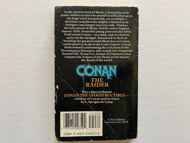 Może przedstawiać: Czarno-biała okładka książki z tytułem "Conan The Raider" w dużych, pogrubionych, ż&oacute;łtych literach. Okładka zawiera r&oacute;wnież tekst "Dodatkowo specjalny bonus! Conan The Indestructible - historia Conana i jego czas&oacute;w autorstwa L. Sprague de Camp".