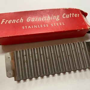 Peut inclure: Une boîte rouge avec du texte blanc qui dit "French Garnishing Cutter Stainless Steel" et un coupe-frites en métal argenté.