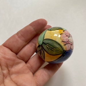 May include: A hand-painted ceramic ornament with a yellow, green, blue, and pink floral design.